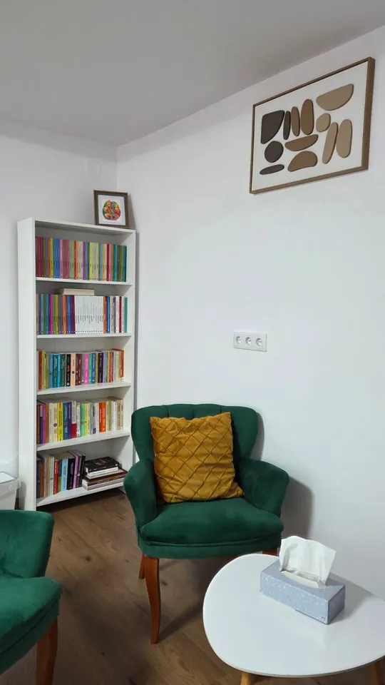 Fotoliu verde de catifea lângă biblioteca cu cărți de psihologie din cabinet