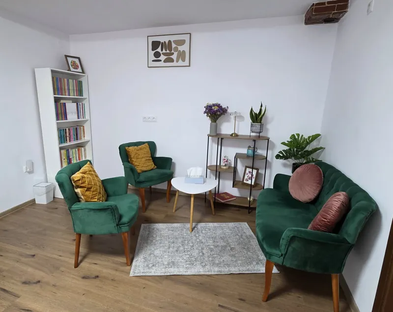 Camera de psihoterapie din cabinetul de psihologie din Sibiu, cu canapea și fotolii verzi de catifea, măsuță și bibliotecă